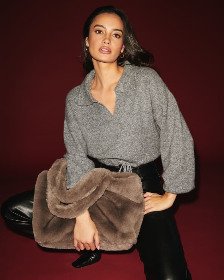A model wears a knit polo sweater and carries a faux fur tote.